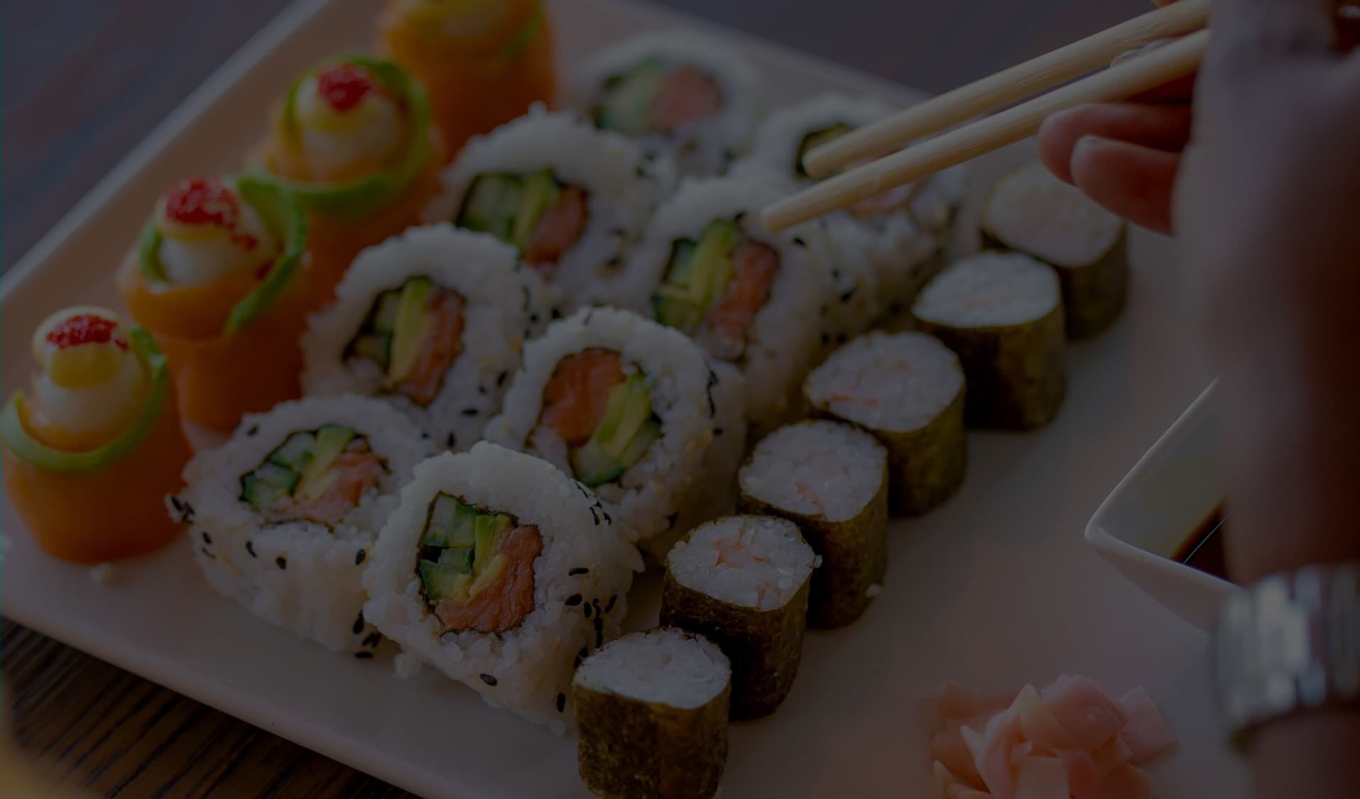 A selection of sushi on a plate with a hand holding chop sticks